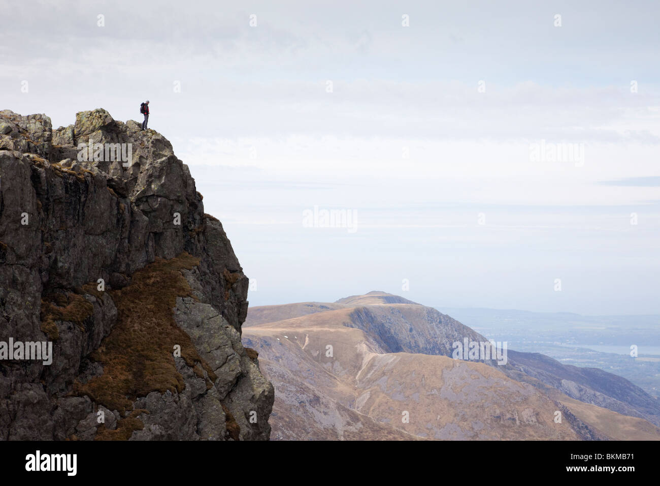 Man standing alone on a craggy mountain top with a view beyond. Glyder Fawr Ogwen Snowdonia National Park North Wales UK Britain Stock Photo