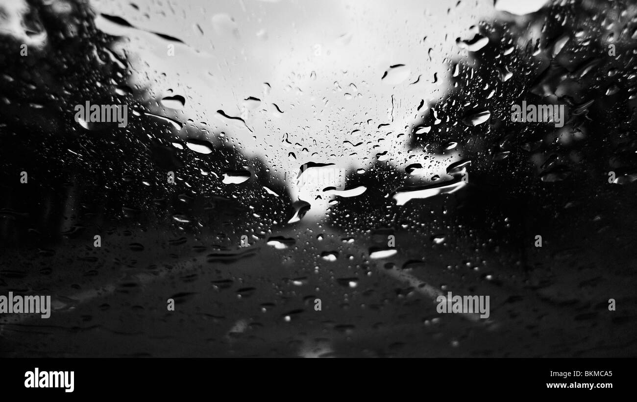 Raindrops on window with blurry road in background. Stock Photo