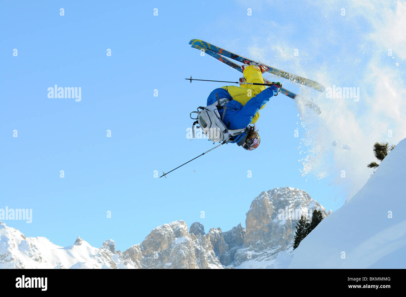 A telemark skier does a front flip as he jumps a drop off piste in the