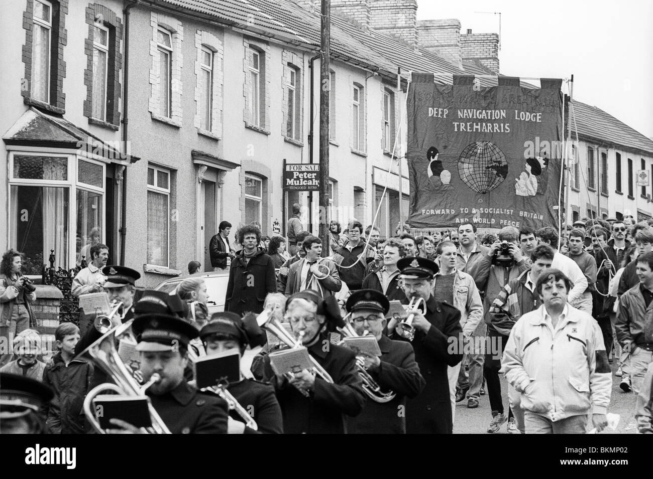 Coal miners and families march through village on last day of work at Deep Navigation Colliery Treharris Glamorgan South Wales Stock Photo