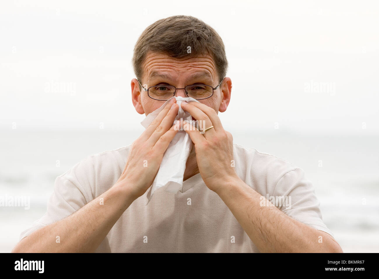 Sneezing mature man in front of the sea Stock Photo