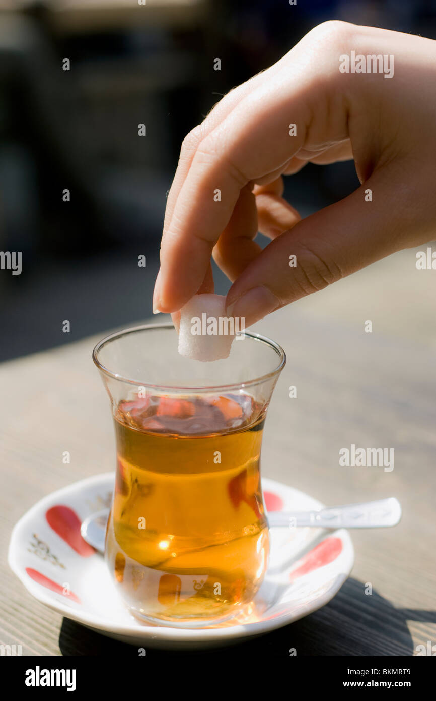 Person adding a sugar cube to a glass of Apple Tea Stock Photo