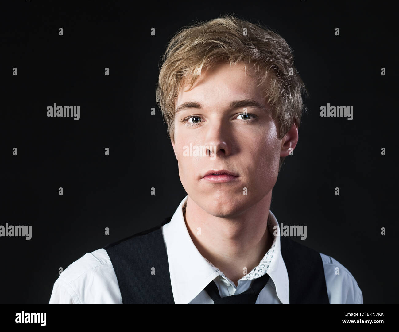Portrait of serious young blond man in white shirt and waistcoat photographed against black background Stock Photo