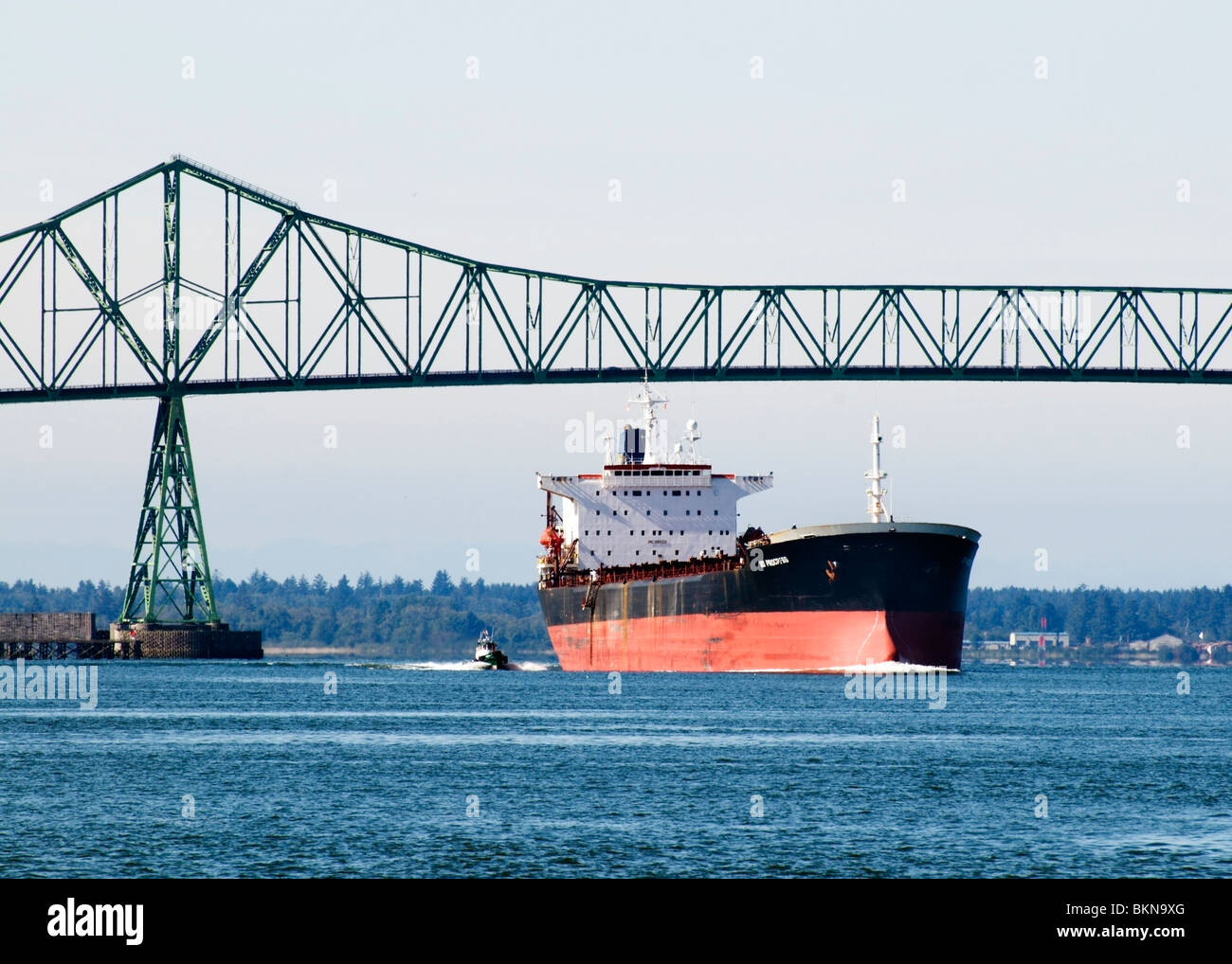 A container ship escorted by a tugboat passes under the Astoria-Megler Bridge in Oregon. Stock Photo