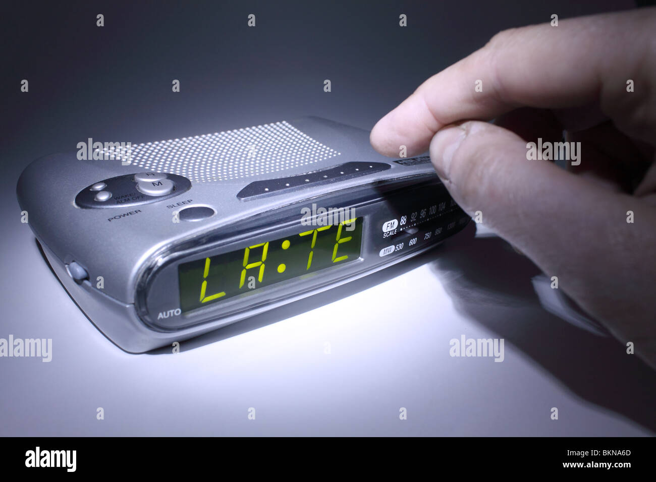 switching off an electronic alarm clock indicating 'LATE' on the digital display Stock Photo