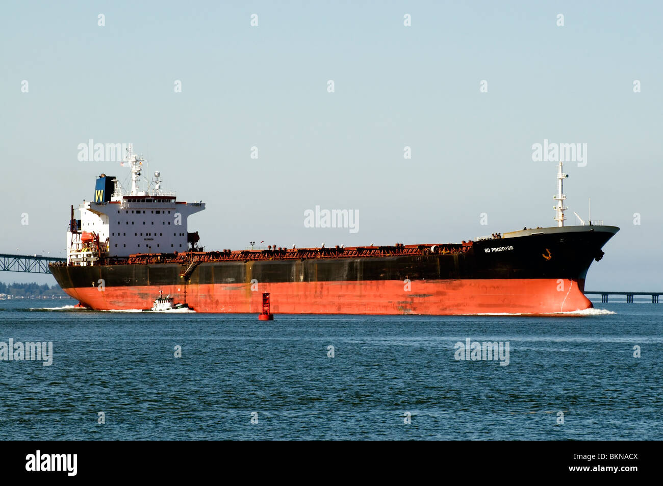 A massive container ship is escorted by a tugboat from the Pacific Ocean into the mouth of the Columbia River in Oregon. Stock Photo