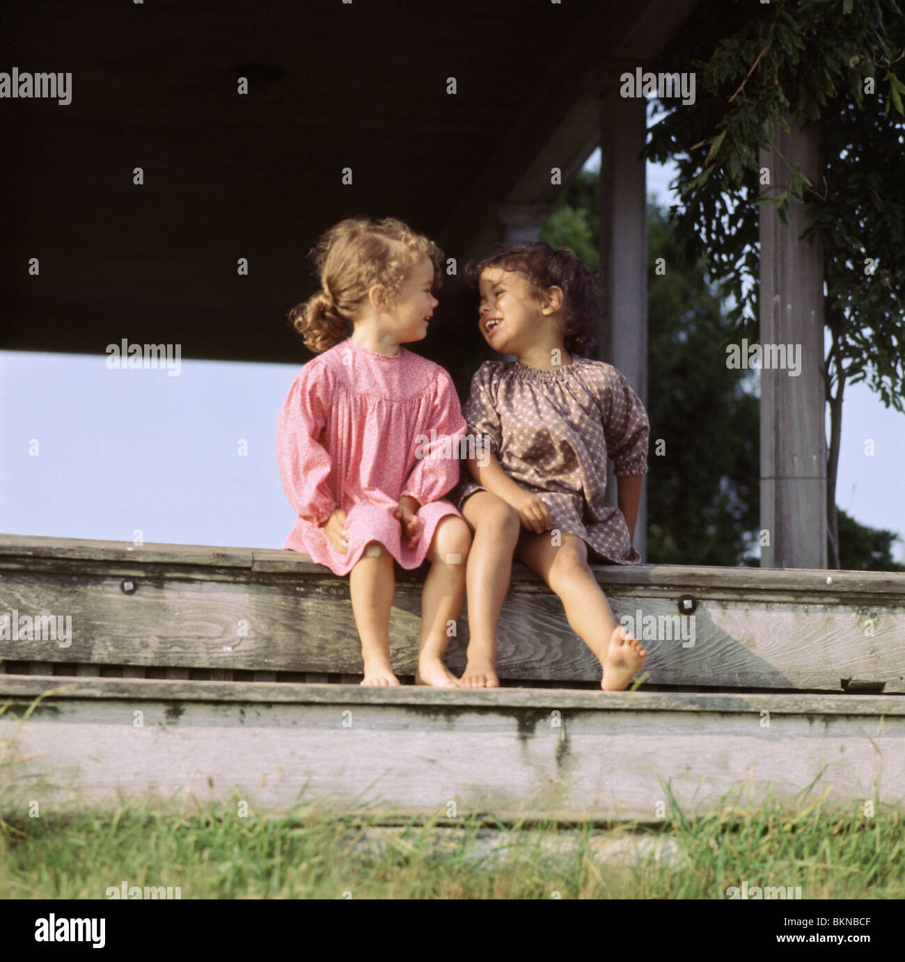 Two young ethnically diverse girls sitting on the steps talking Stock Photo