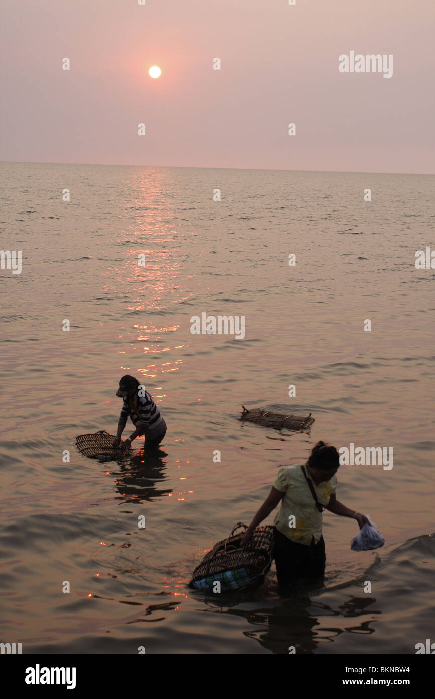 Local women check on the cages of crabs in shallow surf off the coast off Kep, Cambodia Stock Photo