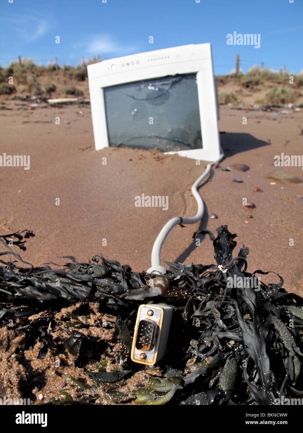 an old washed up analogue computer monitor with rusty cable lying on the beach. Stock Photo