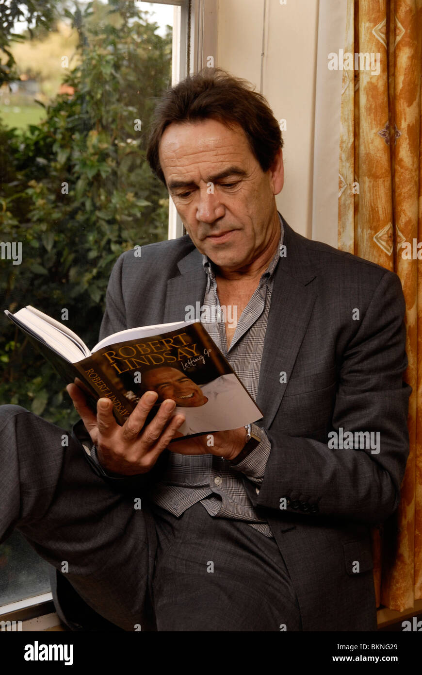 Actor Robert Lindsay reading by a window. He has a purpose built library in his home in Denham Bucks Stock Photo