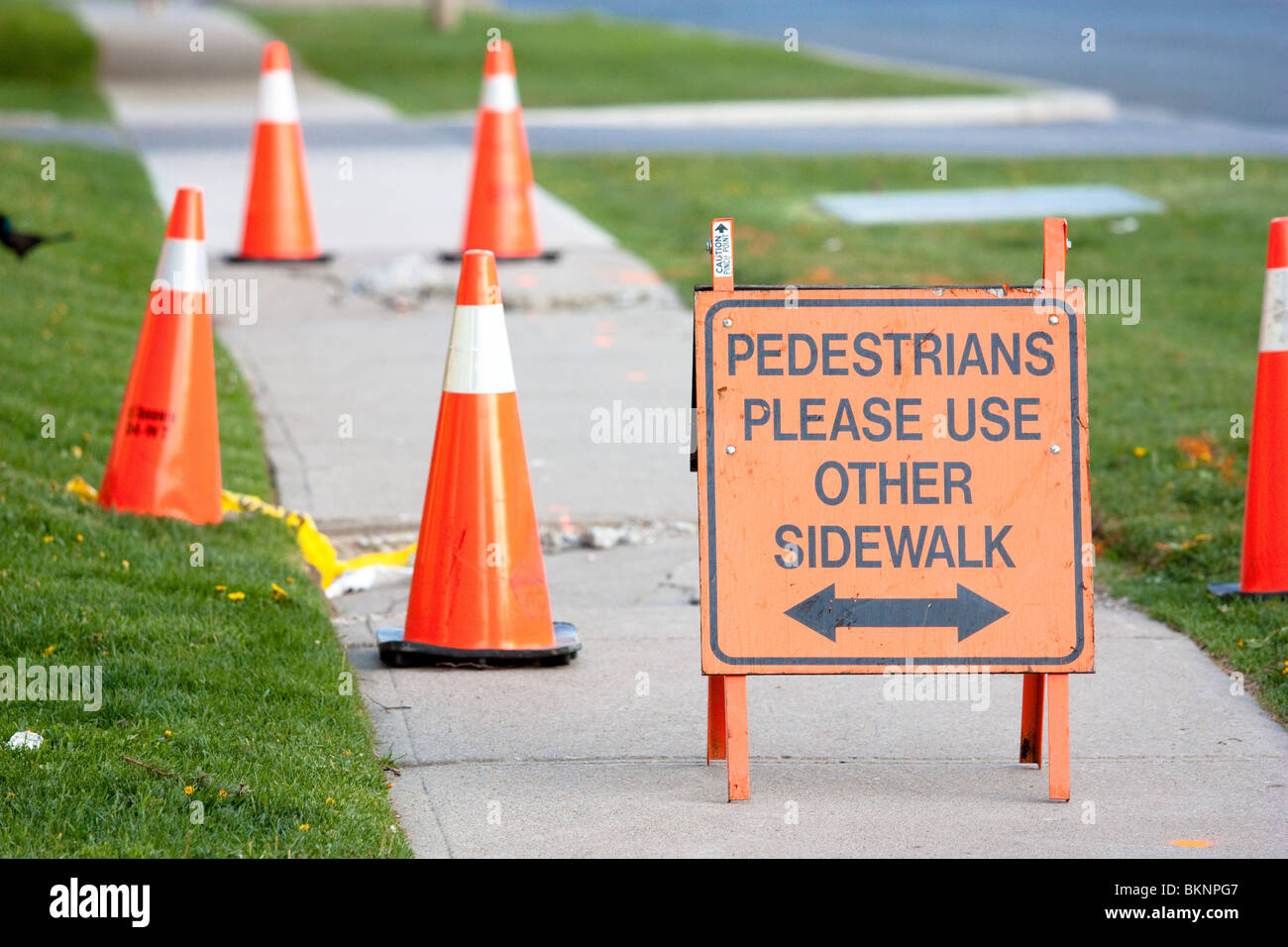 pedestrians please use other side walk orange sign broken road orange cone  cones danger concrete walkway grass Stock Photo