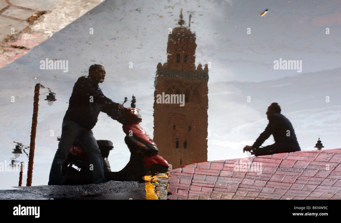 General view of passers by reflected in a puddle whist passing the Koutoubia Mosque in Marrakesh, Morocco. Stock Photo