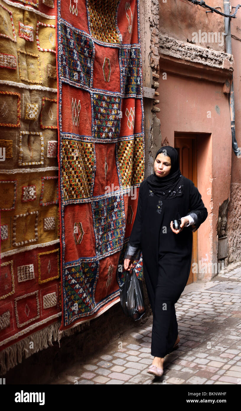 A Muslim woman walks past a Moroccan rug in the Souks of Marrakesh in Morocco. Stock Photo