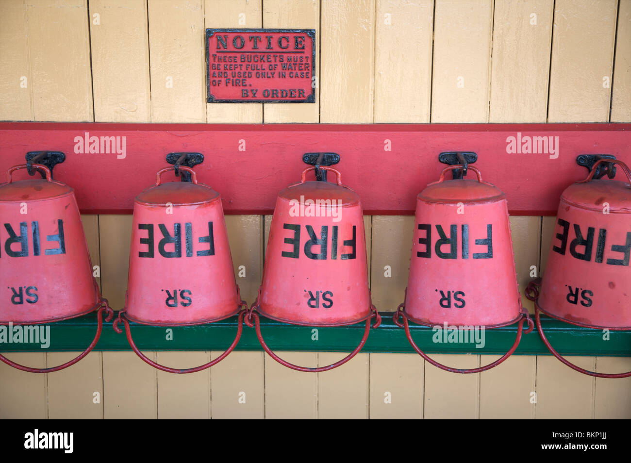 Five red fire buckets empty of water hanging up beside a sign reading