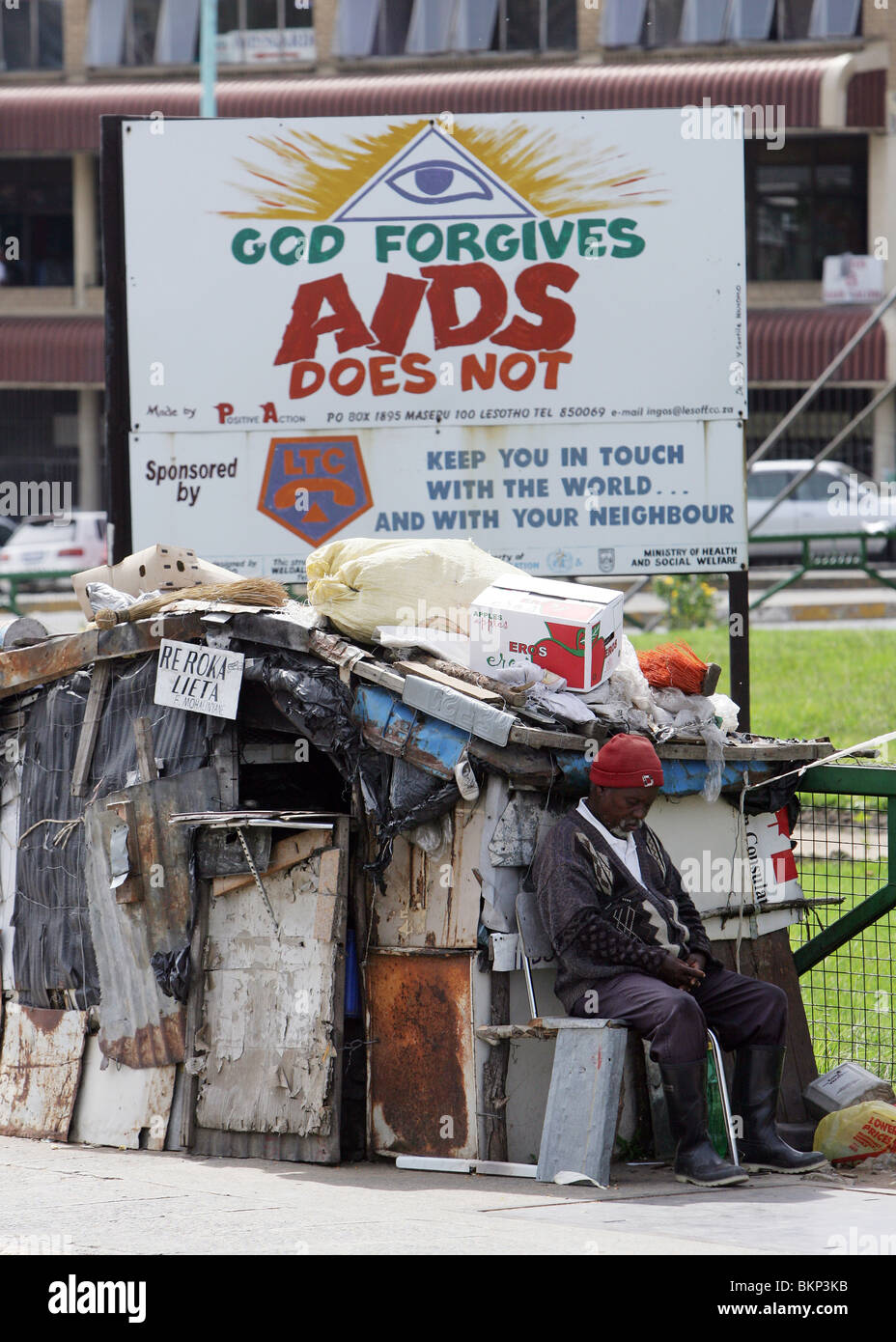 man sitting under a roadside bilboard warning of the dangers of HIV Aids. Maseru, capital of Lesotho Stock Photo