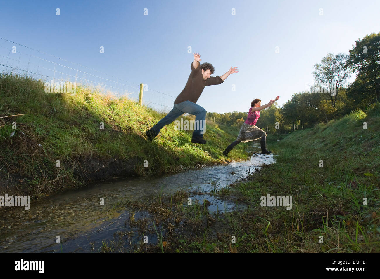 Man en vrouw springen over een slootje. Man and woman jumping over ditch. Ruben Smit Digital Image Archive Stock Photo