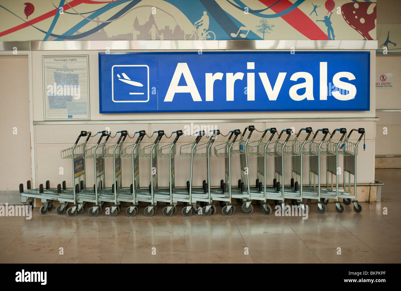 Airport Arrivals sign with row of baggage trolleys Stock Photo