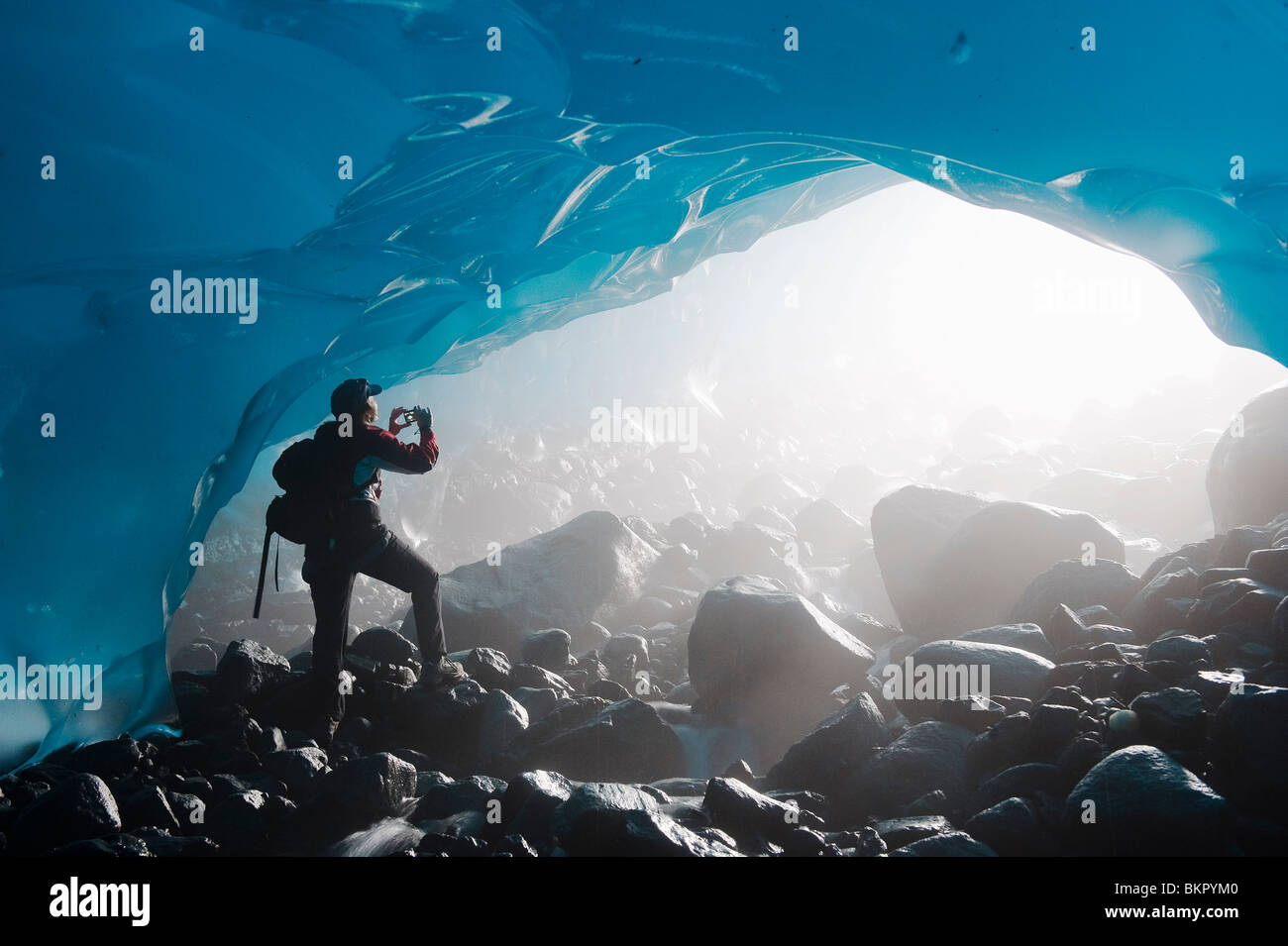 A hiker takes a photograph of the entrance of an ice cave from the inside of the Mendenhall Glacier, Southeast Alaska, Summer Stock Photo