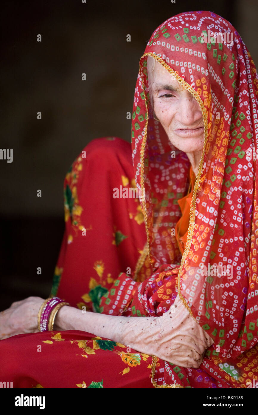 Old Rajasthani woman in a bright red headscarf looking into the  camera. Stock Photo