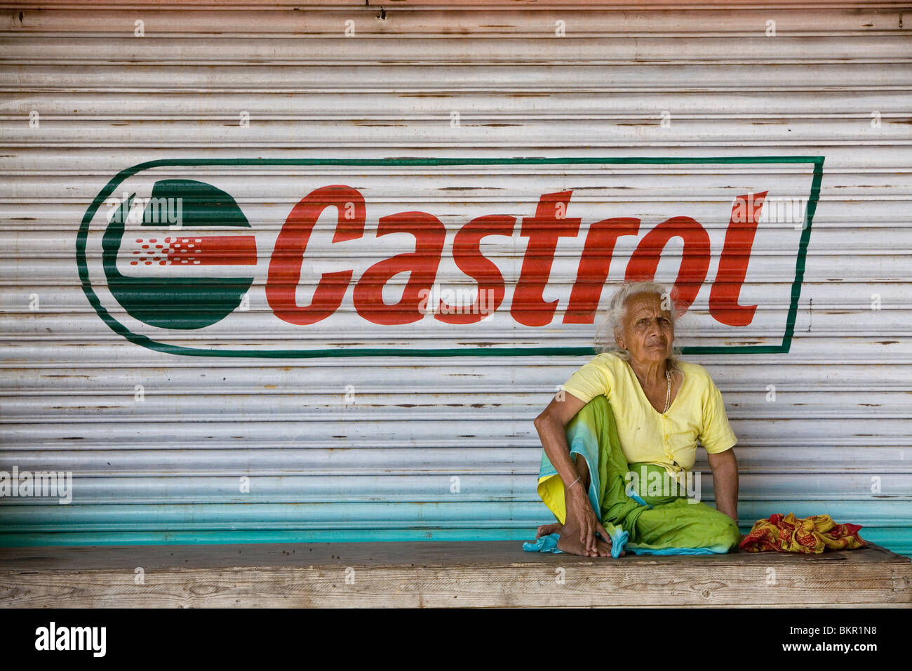 Elderly Rajasthani woman resting in front of a closed shop. Stock Photo