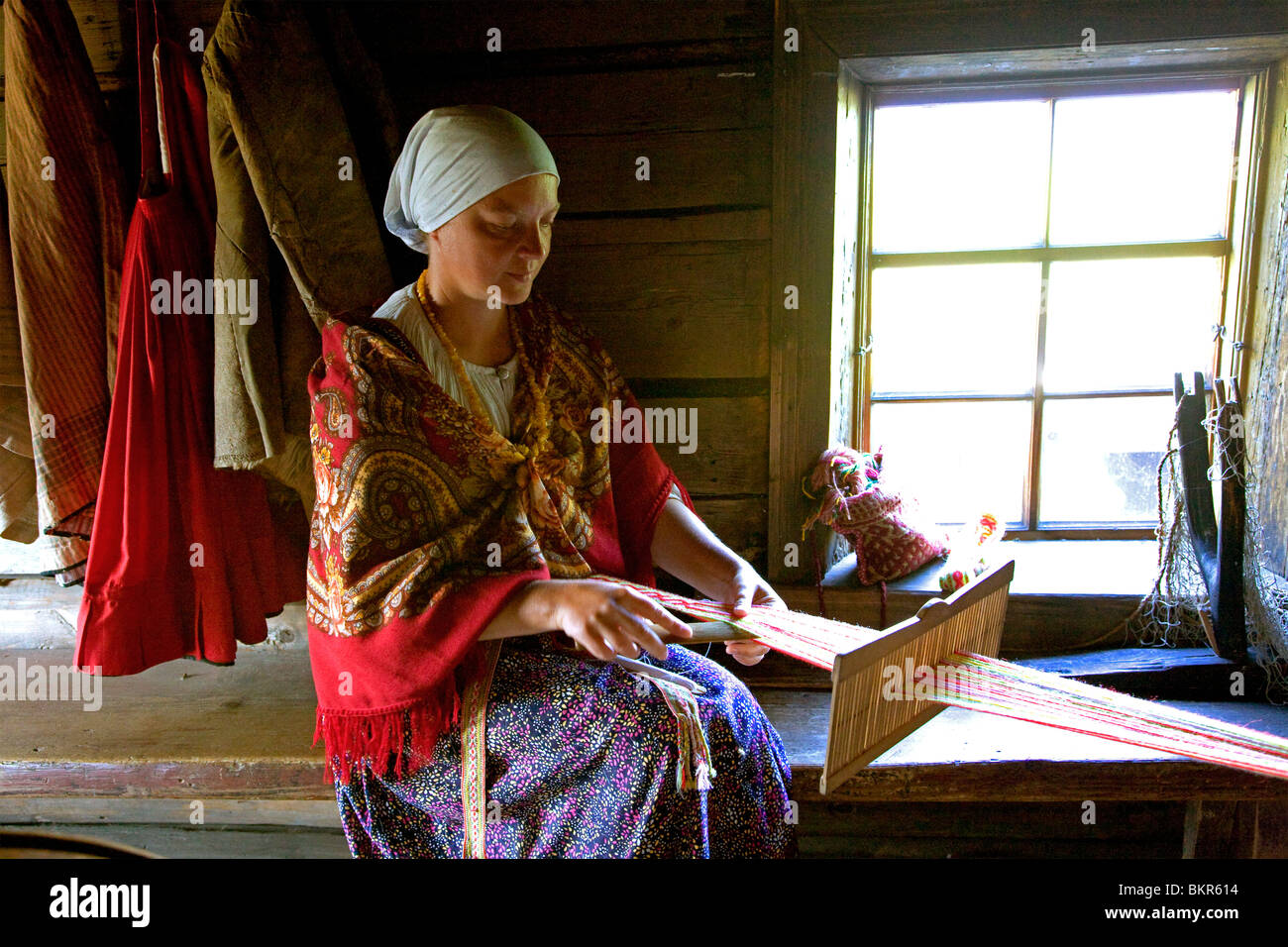 Russia; Karelia; Kizhi Island; Inside a wooden barn, a woman in a peasant costume knitting. Stock Photo