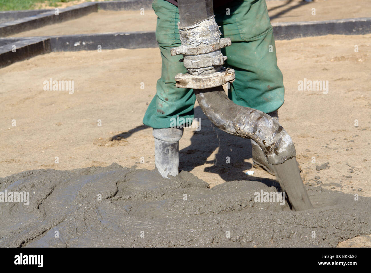 Closeup of construction worker pouring concrete mix from pump onto compacted foundation surface Stock Photo