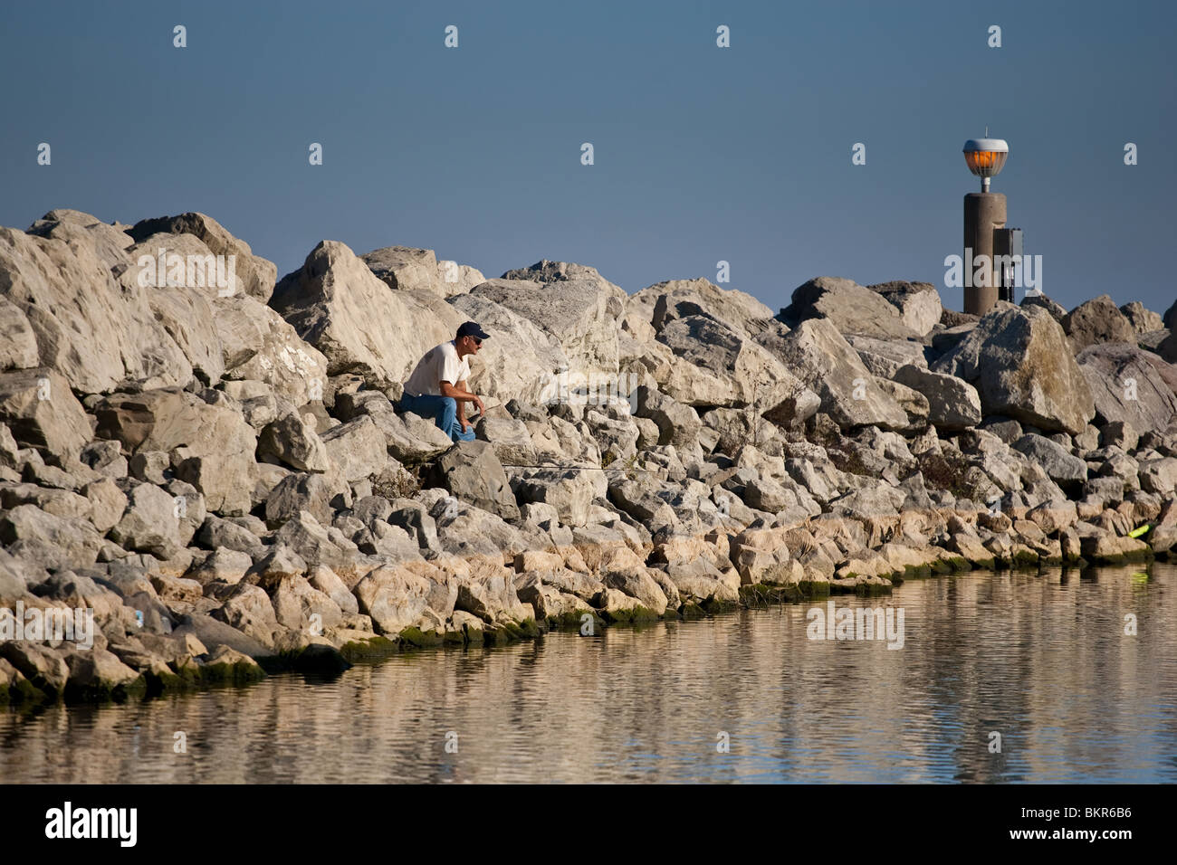 A lone fisherman on a breakwall waiting for his catch to bite, Lake Ontario, Ontario, Canada Stock Photo