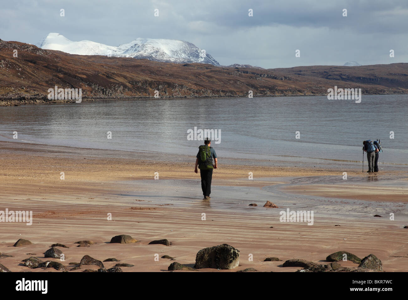Walkers Beachcombing at Red Point with the View Towards the Snow Covered Torridon Mountains Wester Ross West Coast of Scotland Stock Photo