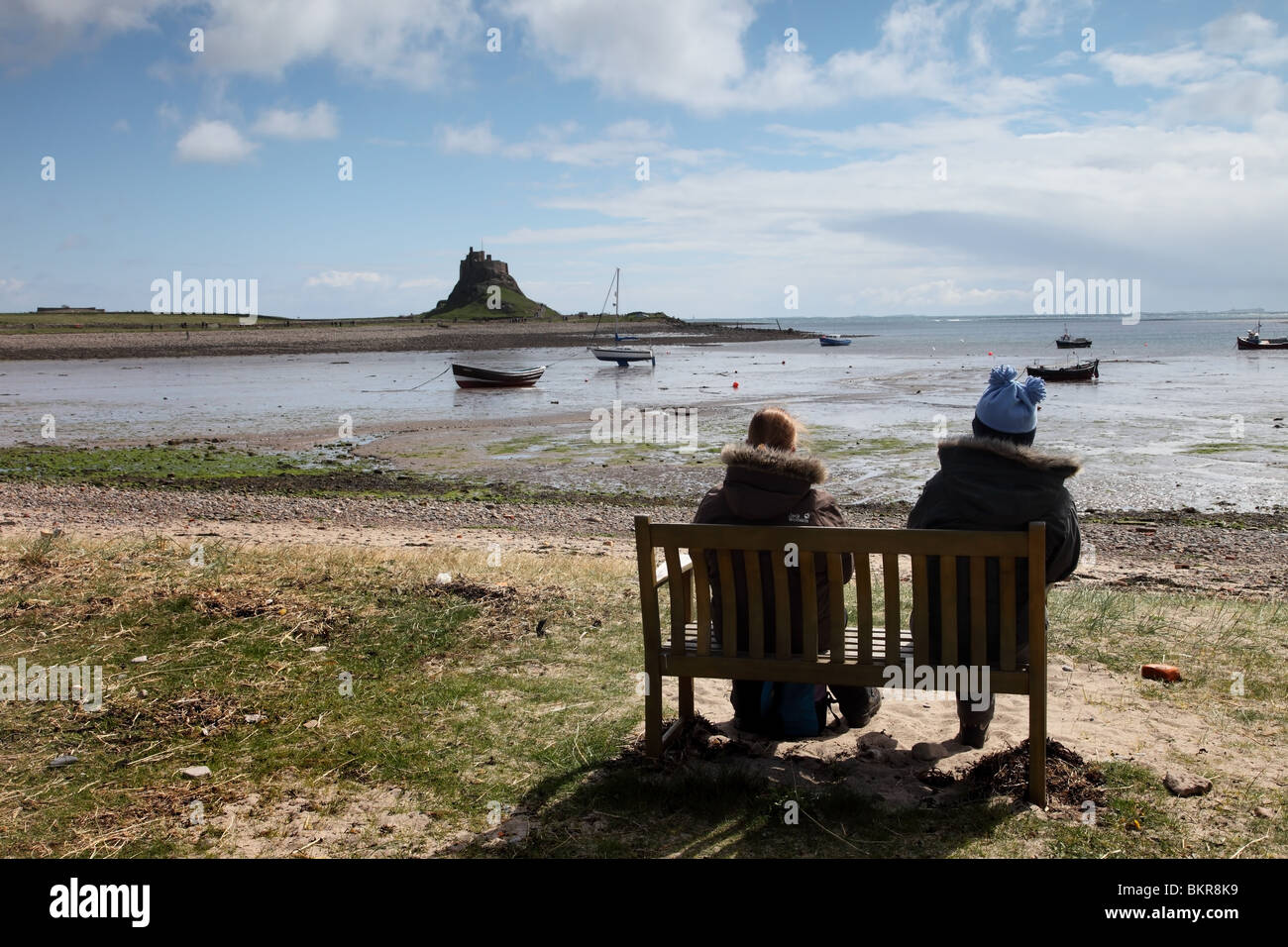 Two People Sitting on a Bench and Enjoying the View of Lindisfarne Castle Holy Island Northumberland Stock Photo