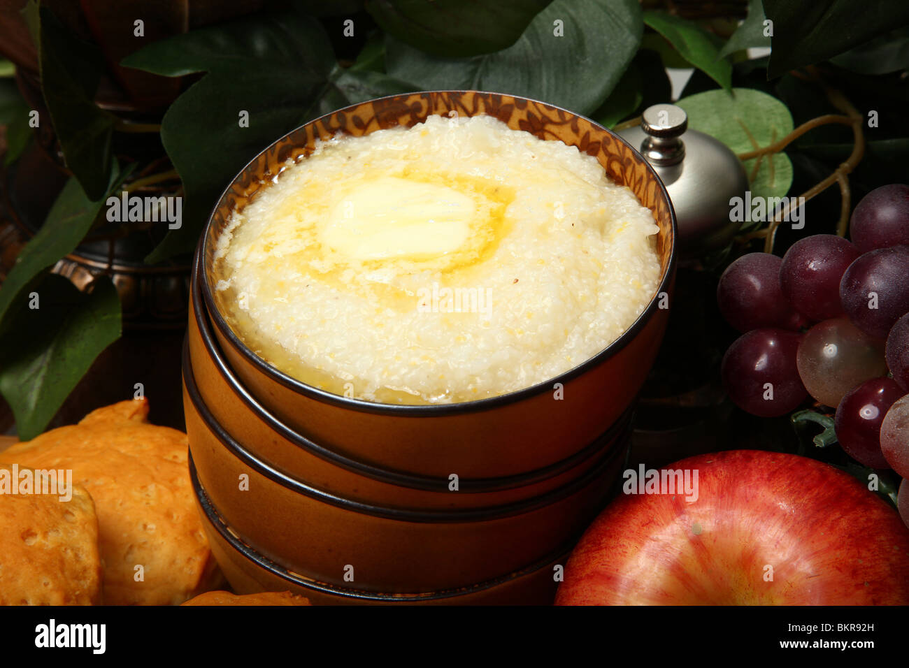 Bowl of hot grits and butter with biscuits and fruit in kitchen. Stock Photo