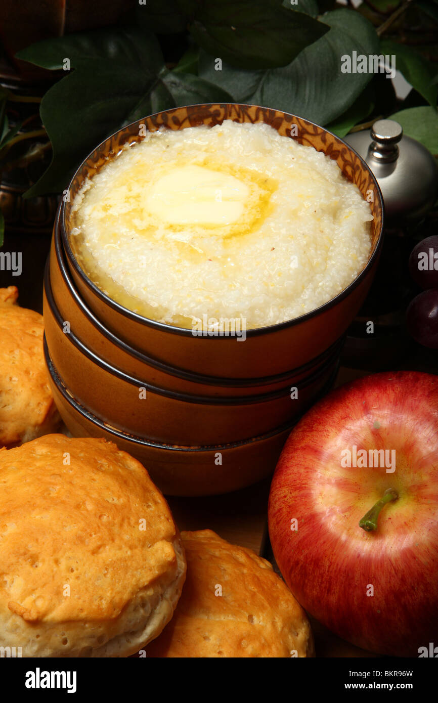Bowl of hot grits and butter with biscuits and fruit in kitchen. Stock Photo