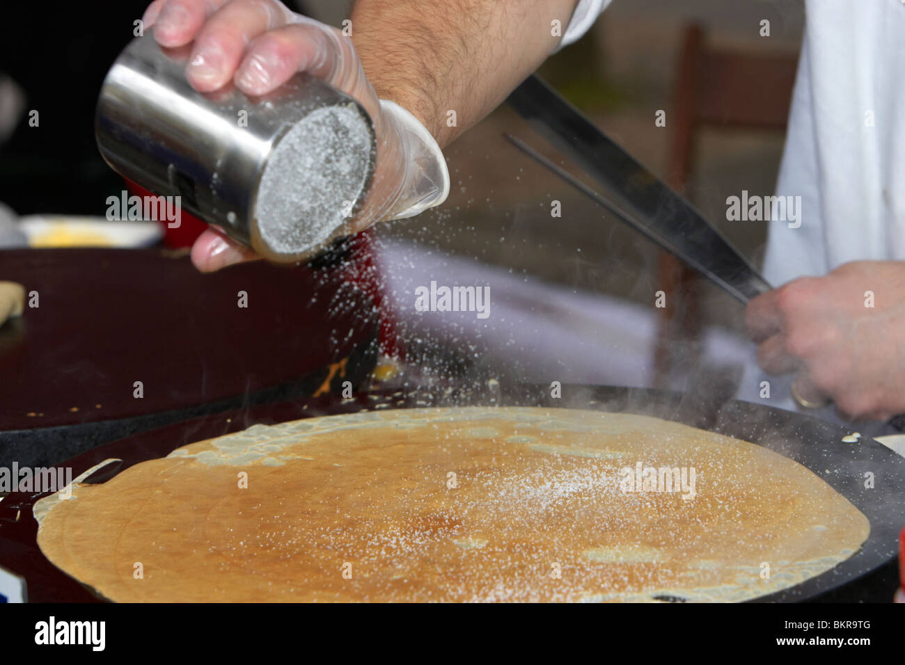 man shaking sugar whilst making crepe pancakes on a fast food stall in a market Holywood County Down Northern Ireland UK Stock Photo