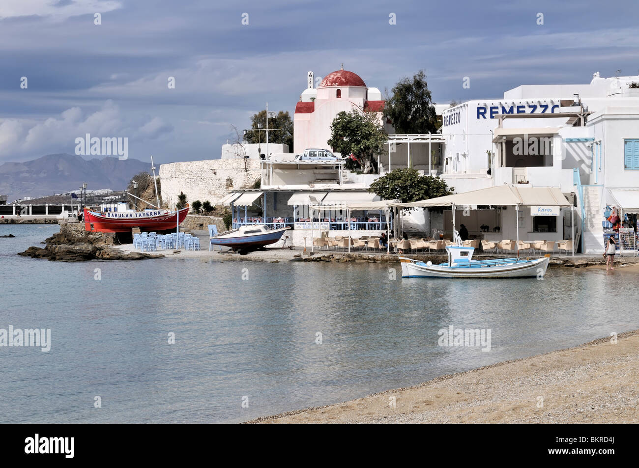 A red domed church, bars and restaurants line the harbor and adjacent beach on Mykonos Island. Stock Photo