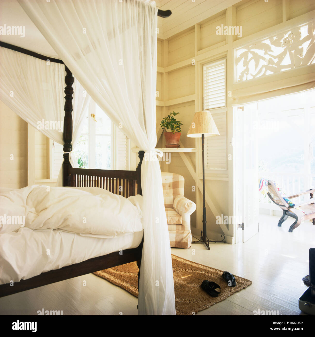 Simple four-poster bed with white voile drapes and linen in white bedroom  with double doors open to veranda Stock Photo - Alamy