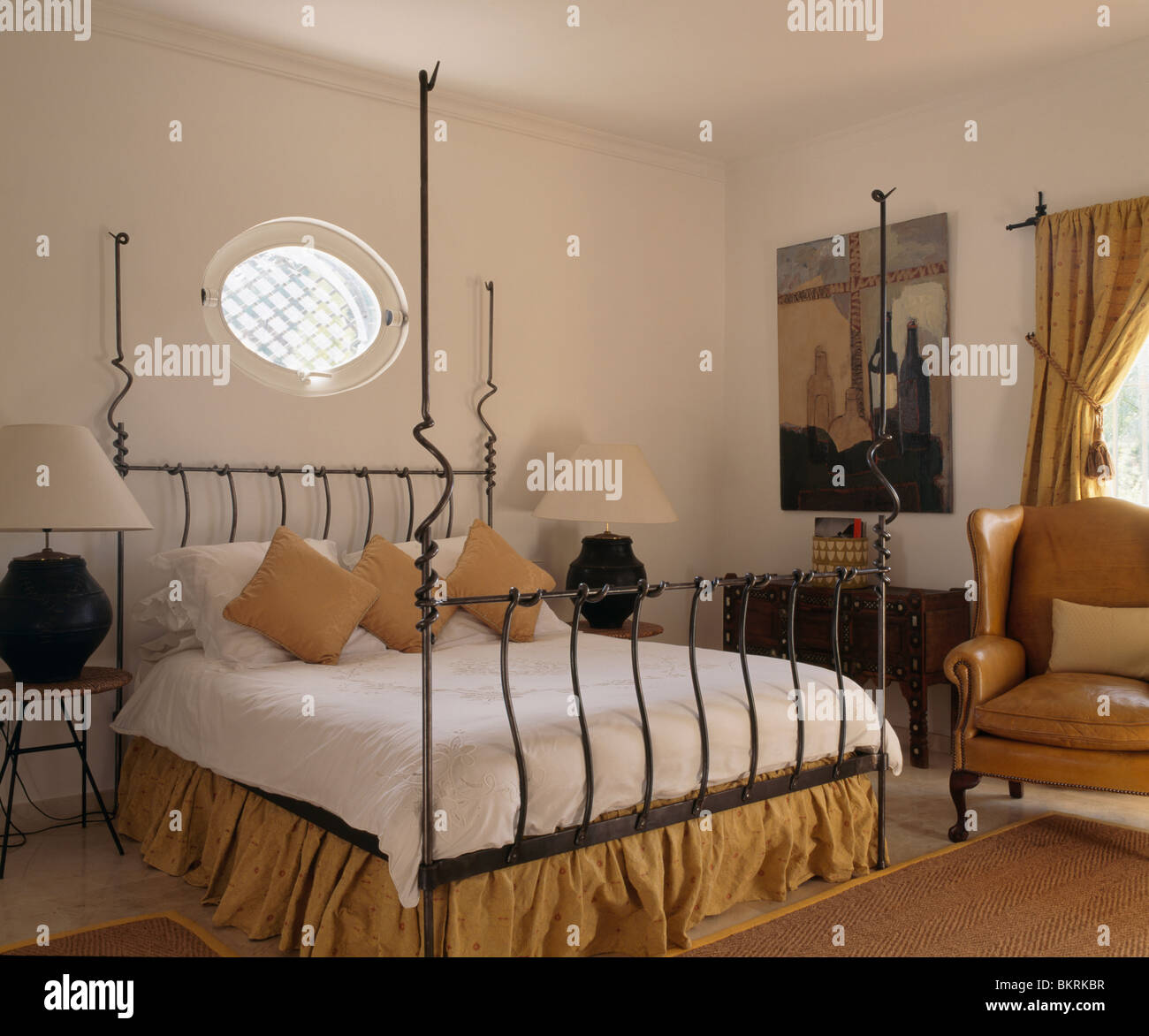 Oval window above modern black wroughtiron bed with white bedcover in
