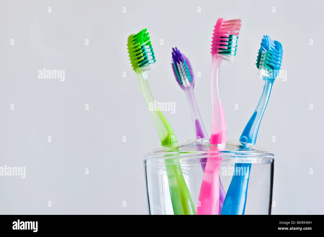 Four different colored toothbrushes in family toothbrush holder. Stock Photo