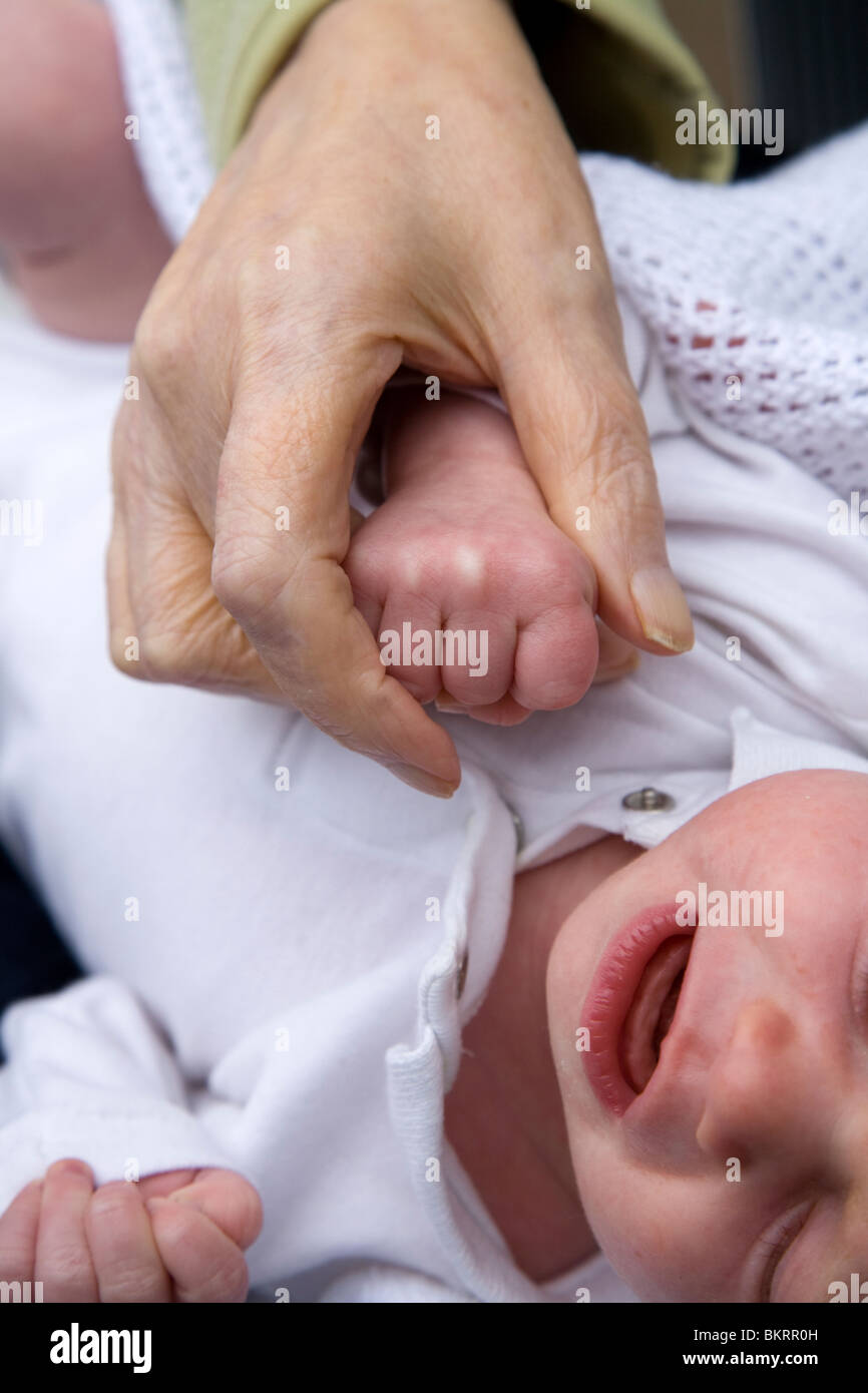 Close up of an older woman's hand holding the hand of a newborn / new born baby. Stock Photo