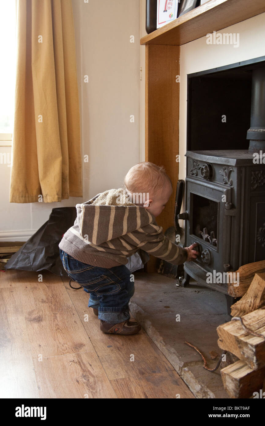 Baby boy ( 1 year old ) playing with a wood burning stove. Hampshire, England. Stock Photo