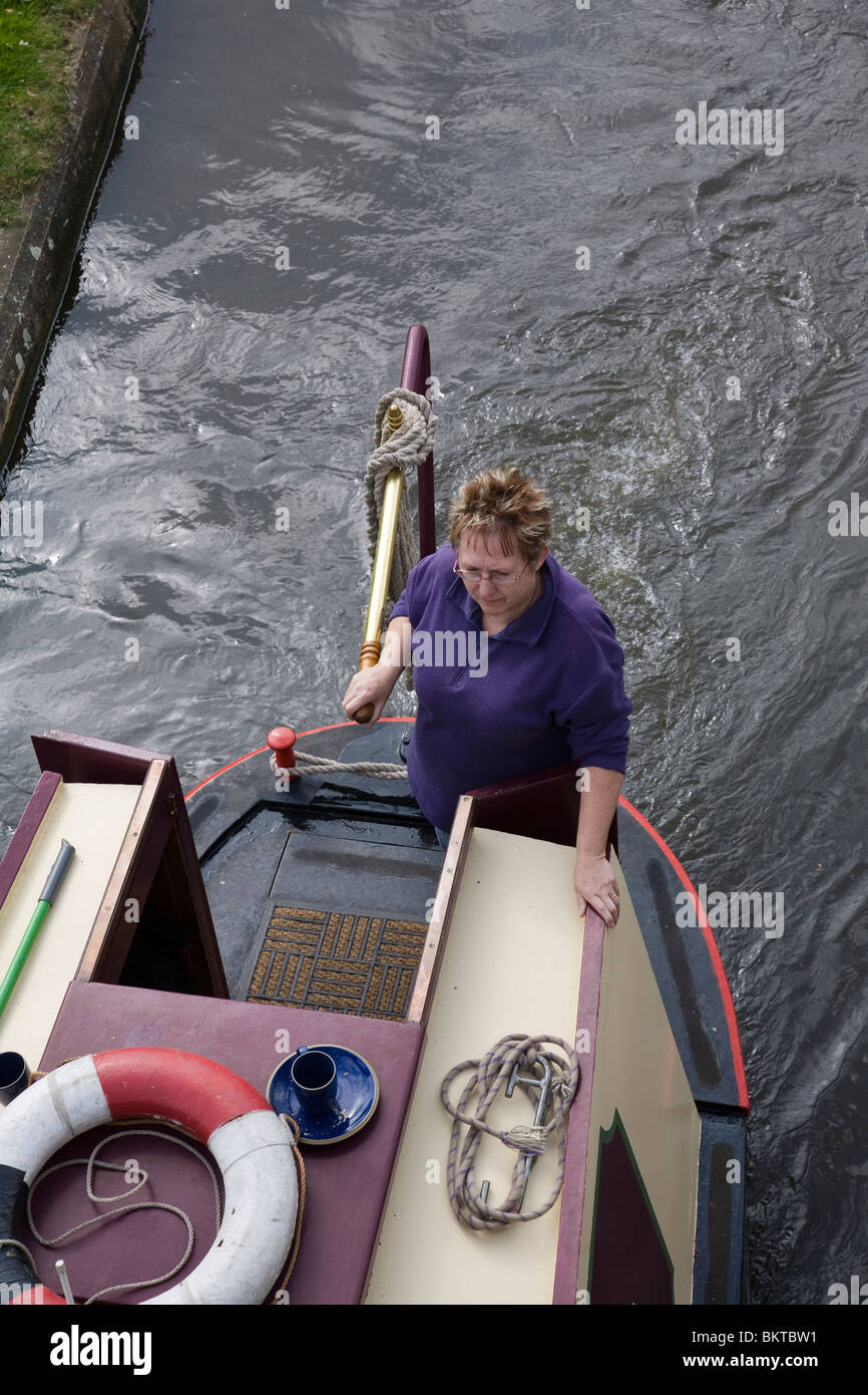 A woman at the tiller of a canal narrow boat as it passes under a ...