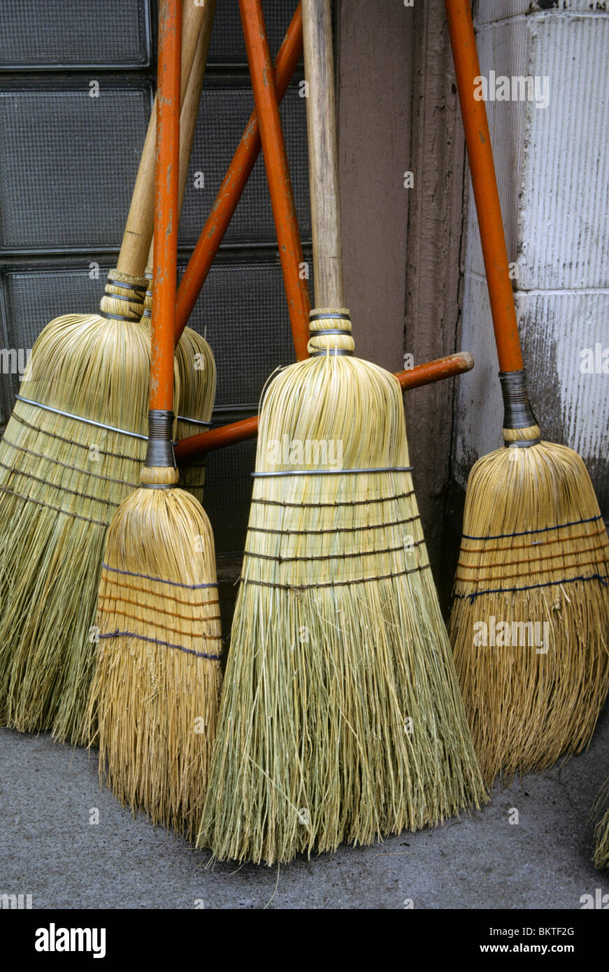 Five mixed heavy duty and medium duty corn brooms of various shapes and sizes leaning against a wall. Stock Photo