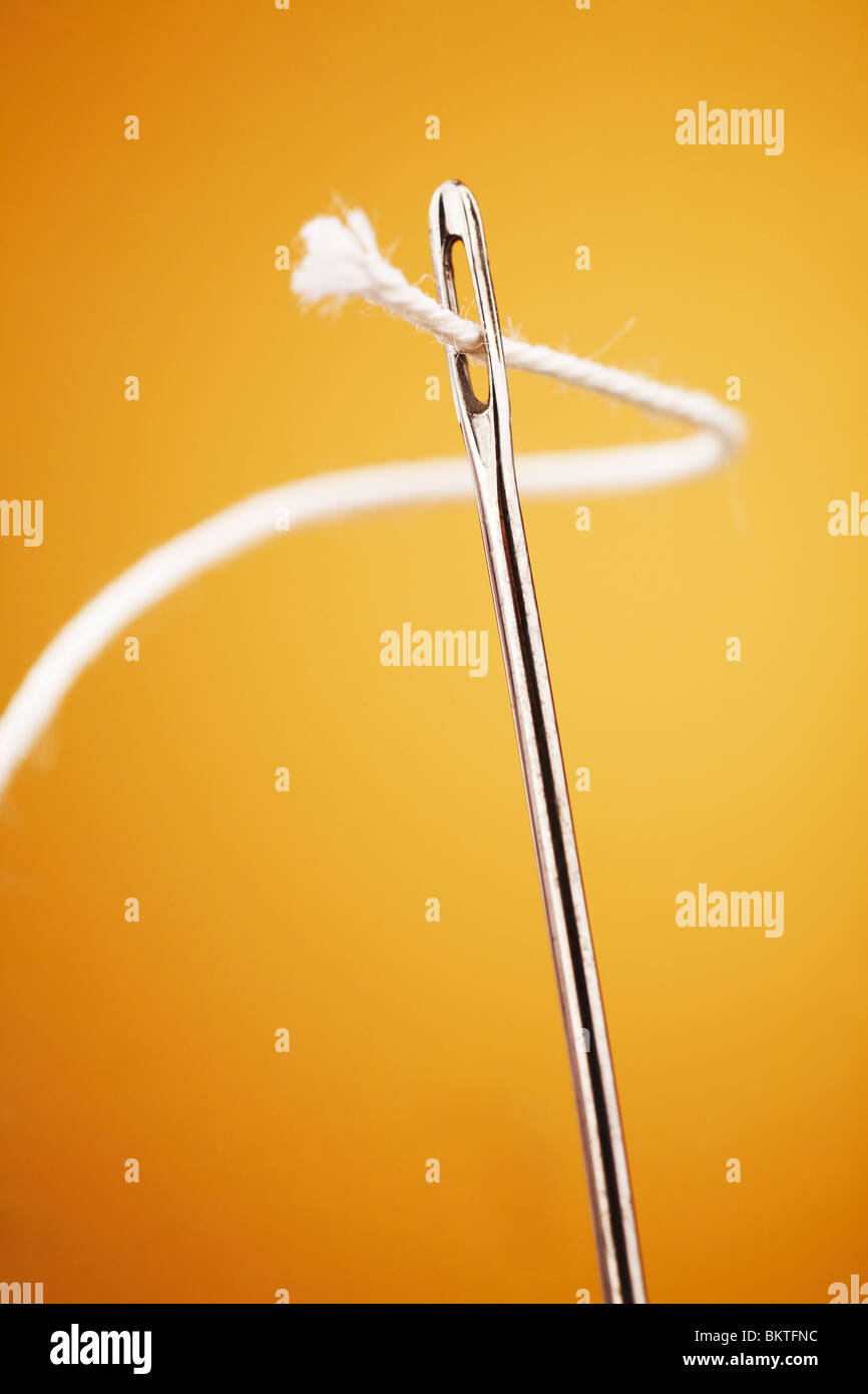 White thread going through needle eye closeup on yellow background Stock Photo Alamy