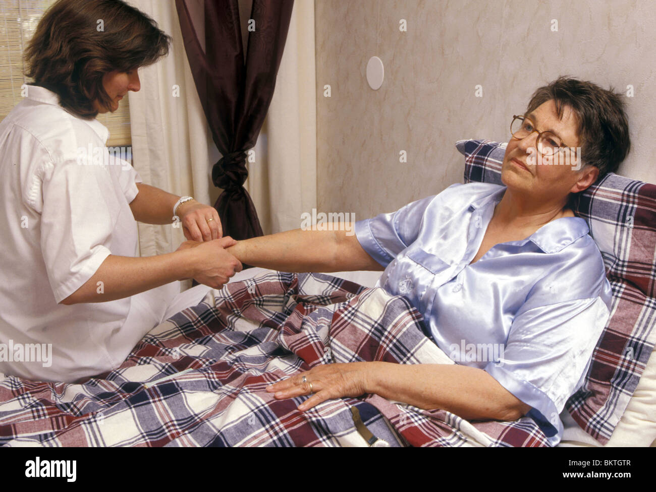 Checking pulse rate: Elderly carer taking pulse beats from sick woman in bed. Stock Photo
