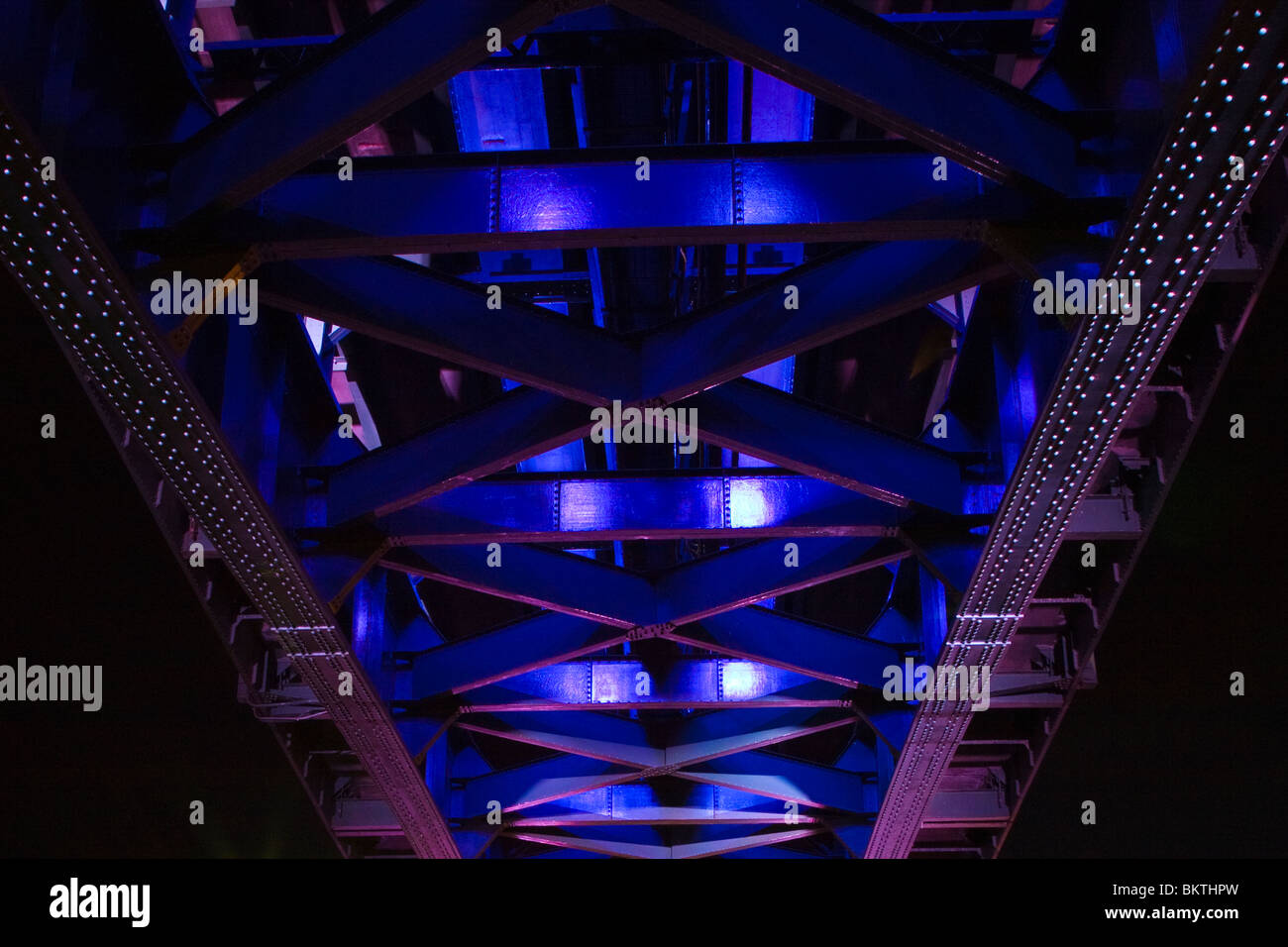 Abstract view of understucture of steel bridge girders lit at night in purple and blue colors Stock Photo
