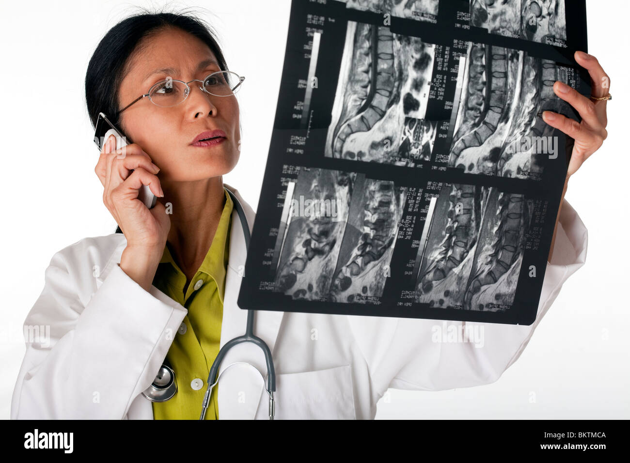 Asian female doctor looking at an MRI scan while talking on a cellphone. Horizontal shot. Isolated on white. Stock Photo
