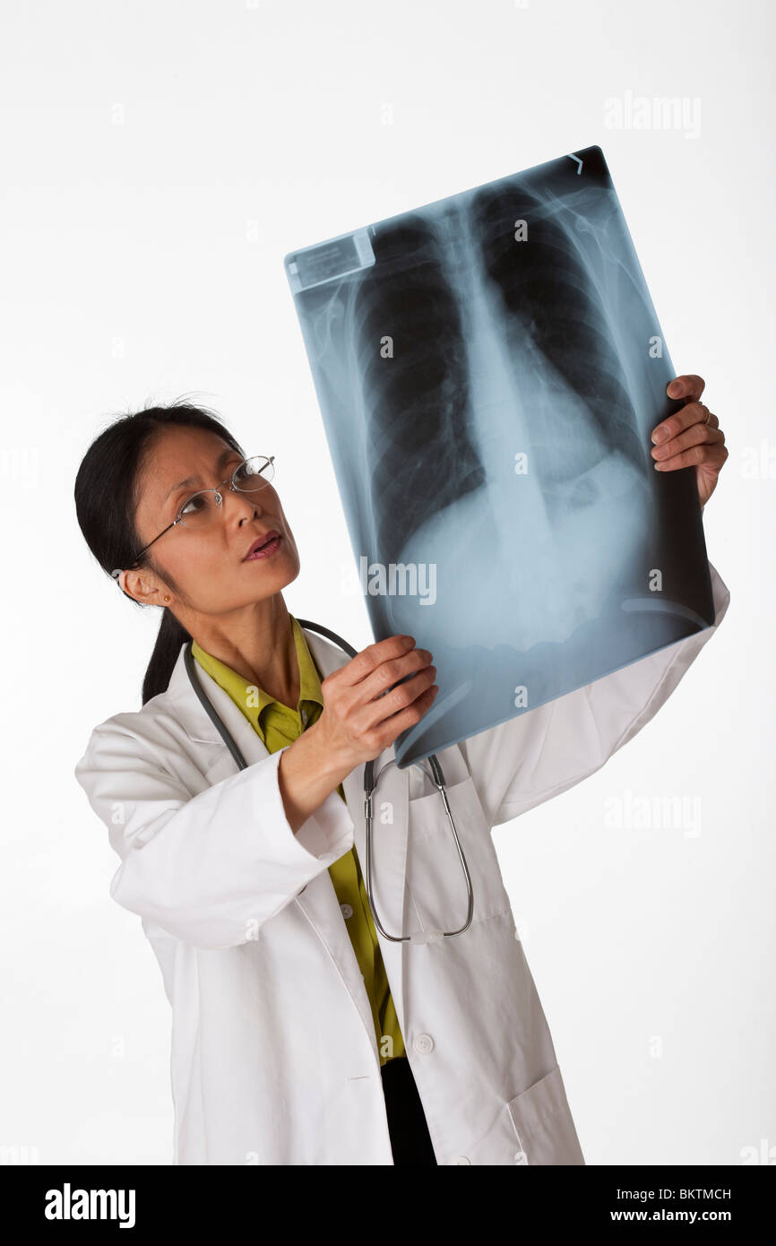 High angle view of an Asian female doctor looking at an x-ray of lungs. Vertical shot. Isolated on white. Stock Photo