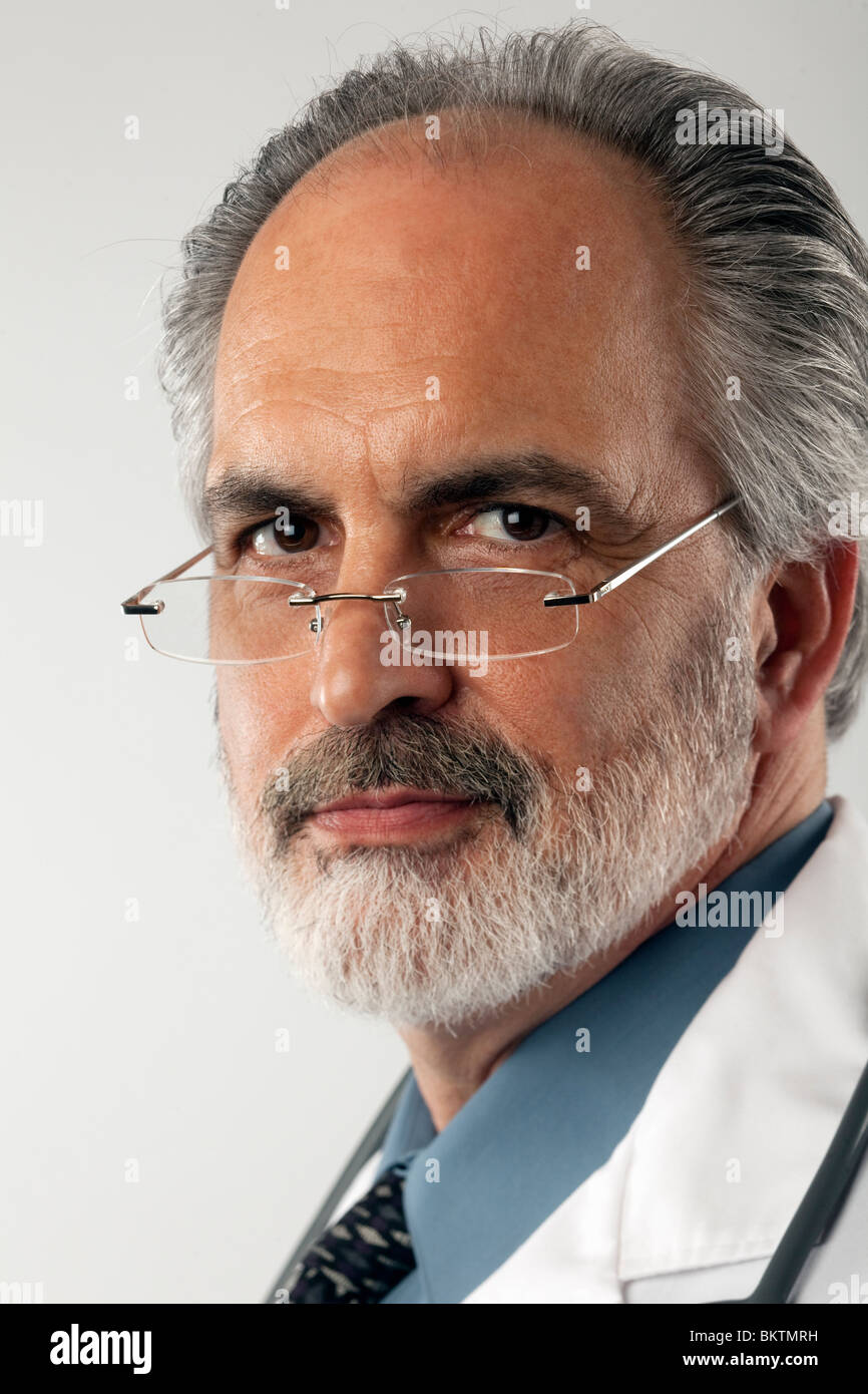 Close-up portrait of a doctor wearing glasses and a white lab coat. He is looking at the camera with a serious expression. Stock Photo