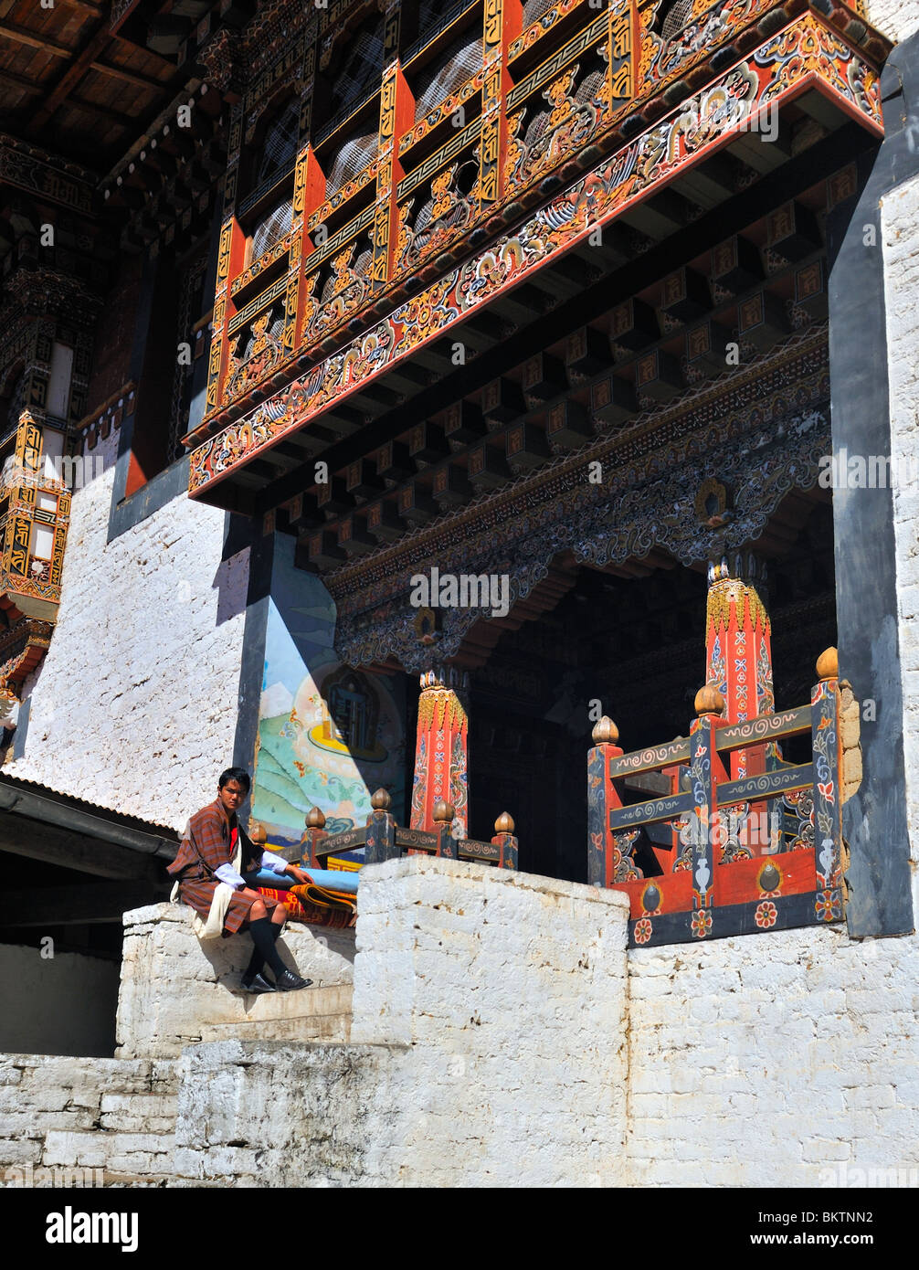 Man in National Dress sitting outside temple entrance Trongsa Dzong Bhutan Stock Photo