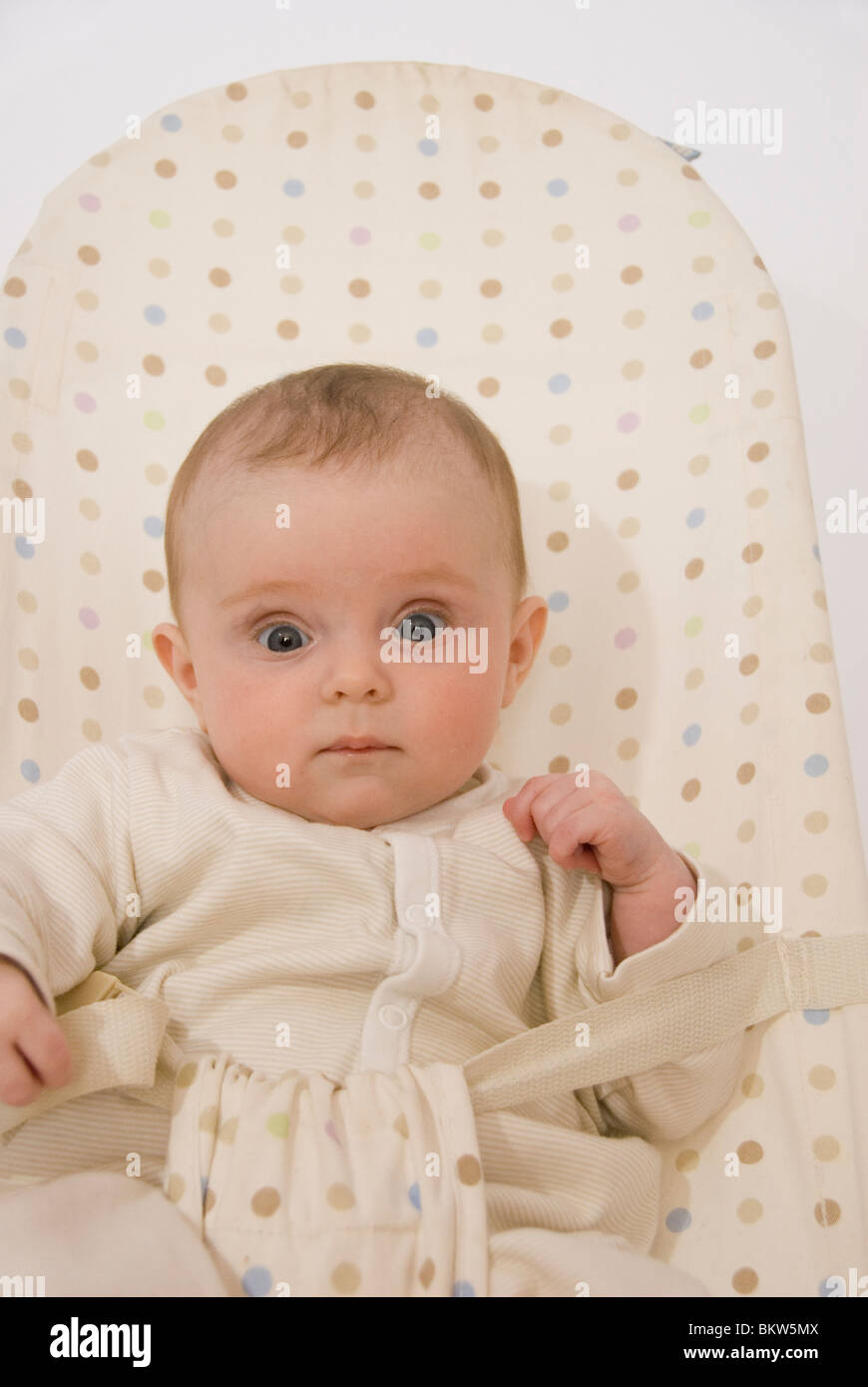 Close Up on Face and Hands of Baby Girl Sitting in Spotted in Bouncer Chair Stock Photo