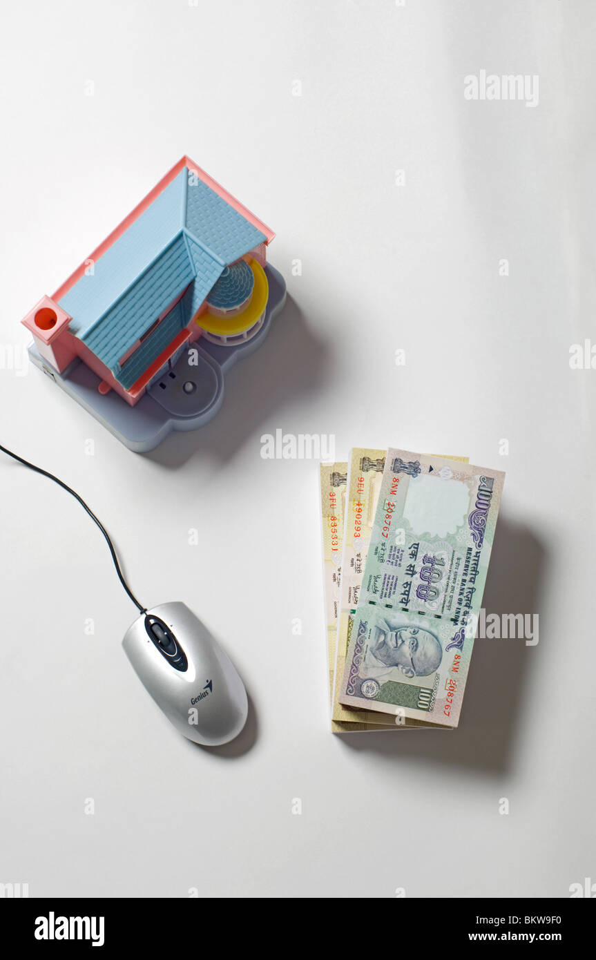 Bundle of Indian rupees bank note, doll house and computer mouse Stock