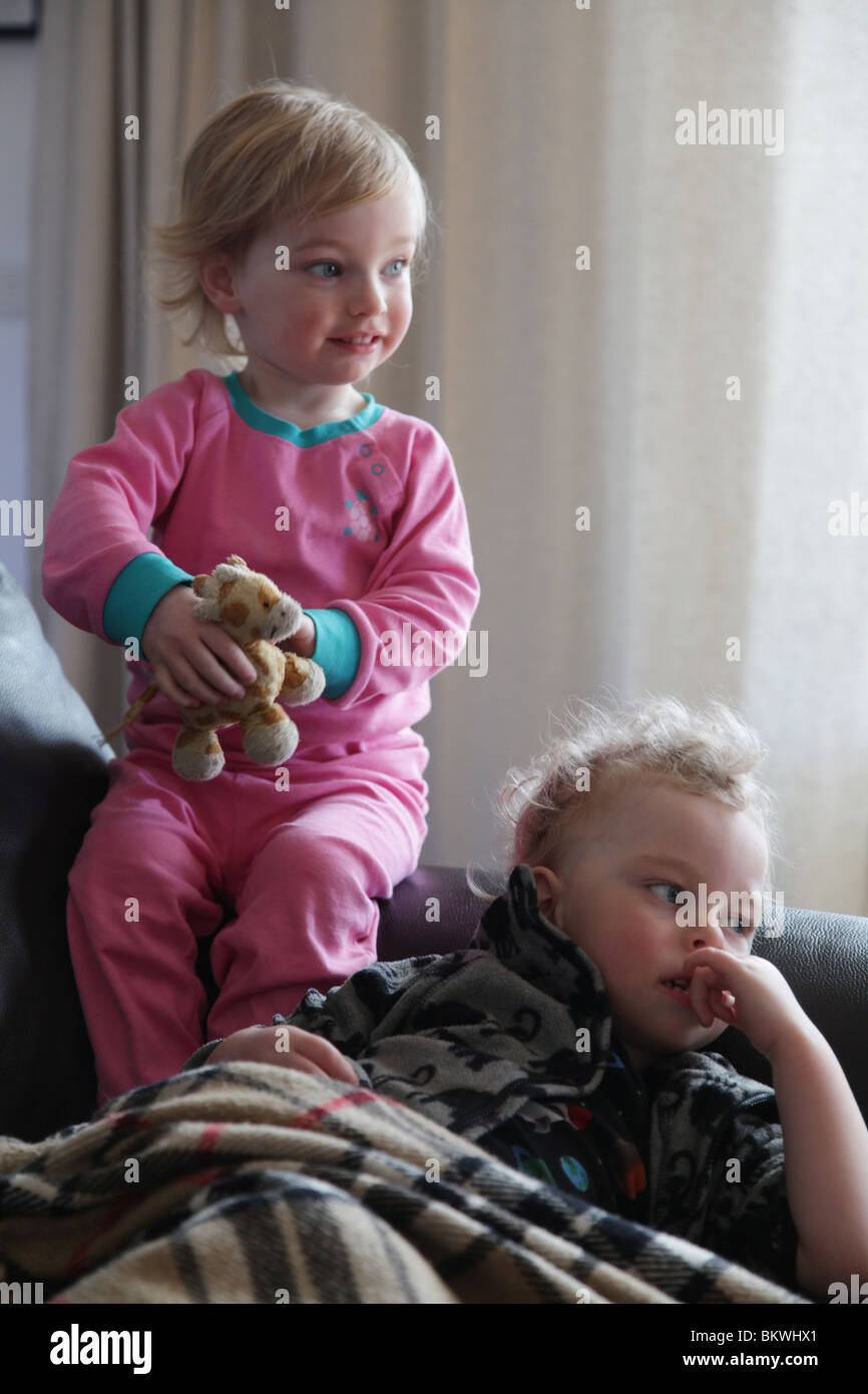 SIBLINGS TOGETHER: Sibling siblings brother sister child children boy girl sit sitting sat sofa couch soft toy hold holding pyjamas Model released Stock Photo